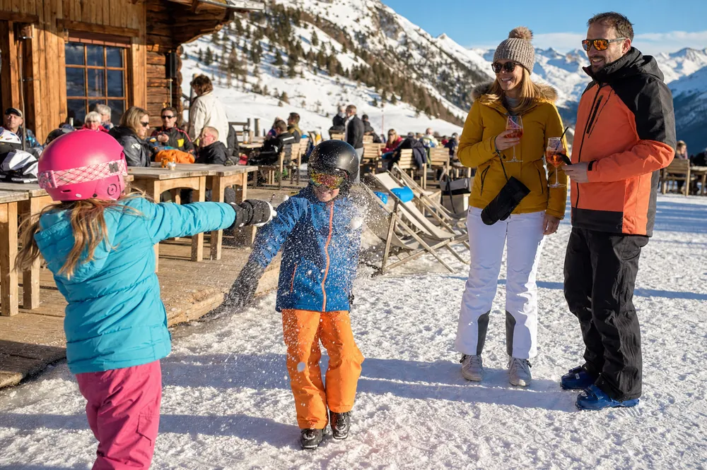Børn med skihjelm leger i sneen uden for en bjergrestaurant