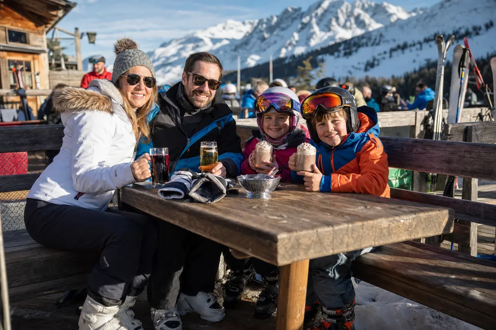 Familie med varm kakao på en solrig terrasse ved pisten